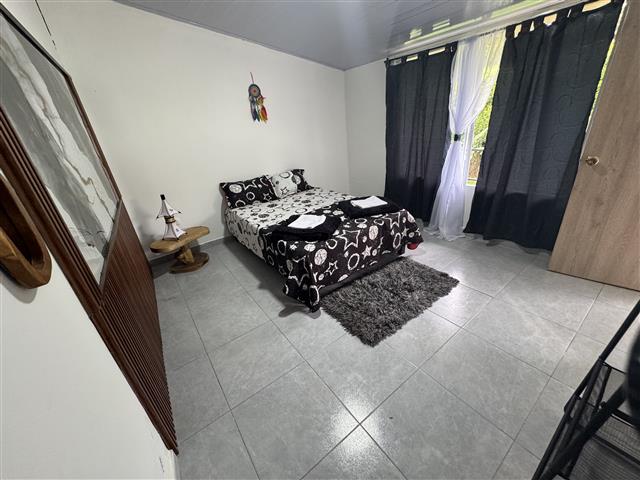 eco-hotel-gaia-11 - Alquiler de Fincas en el Quindio, Hoteles en el Eje Cafetero Small bedroom with a double bed, black-and-white floral bedding, a gray shag rug, and dark window curtains to the right.